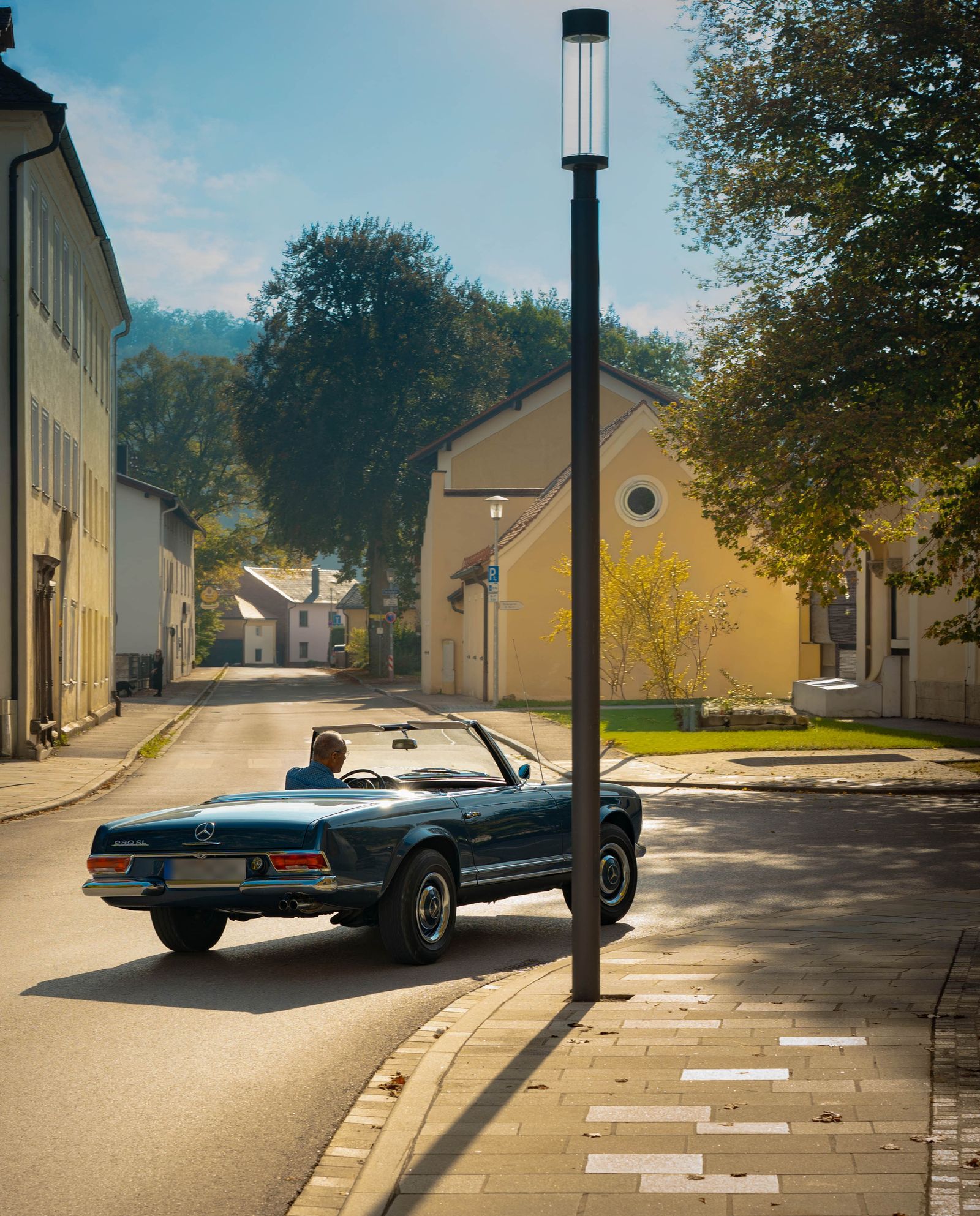 Blaues Oldtimer-Cabrio biegt im Sonnenlicht in eine ruhige Altstadtgasse