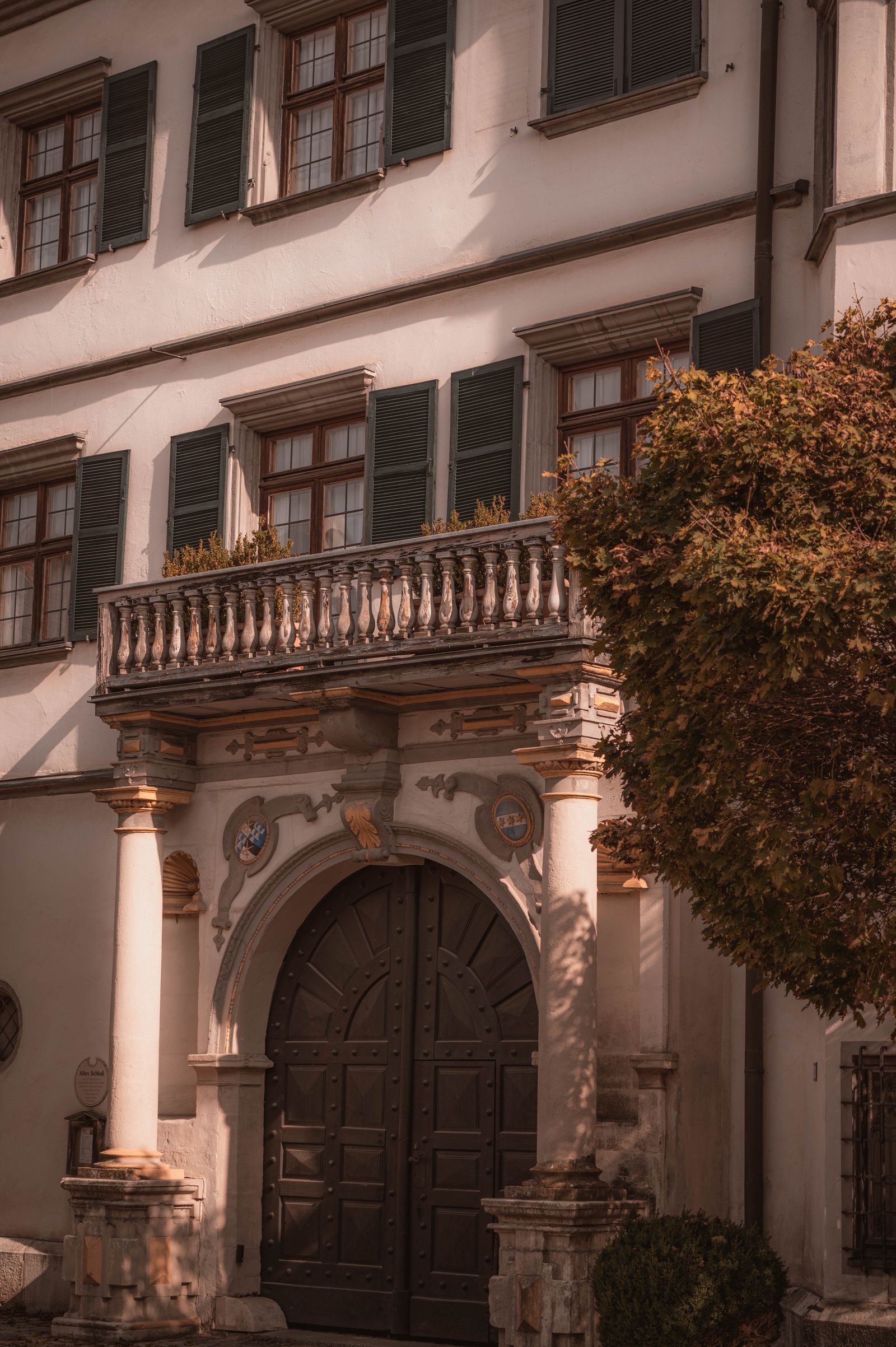 Verziertes Schlossportal mit Säulen, Balkon und grünen Fensterläden in warmem Licht