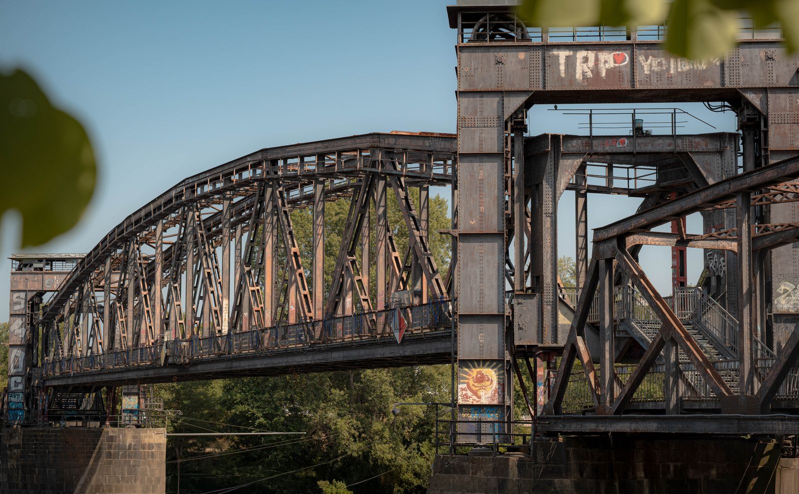 Alte genietete Stahlbrücke mit Graffiti hinter unscharfem Laub