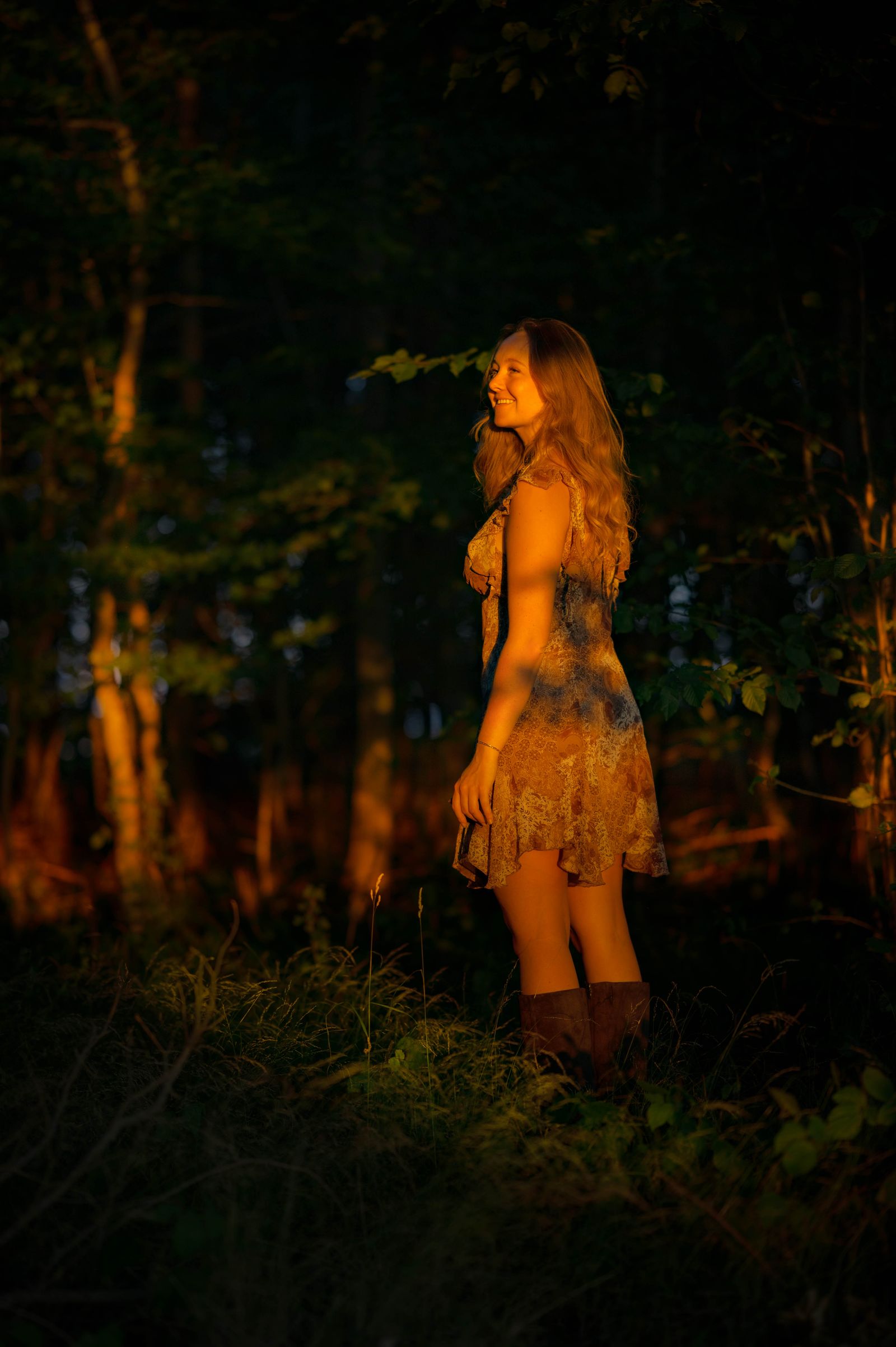 Frau im geblümten Kleid im goldenen Abendlicht am Waldrand